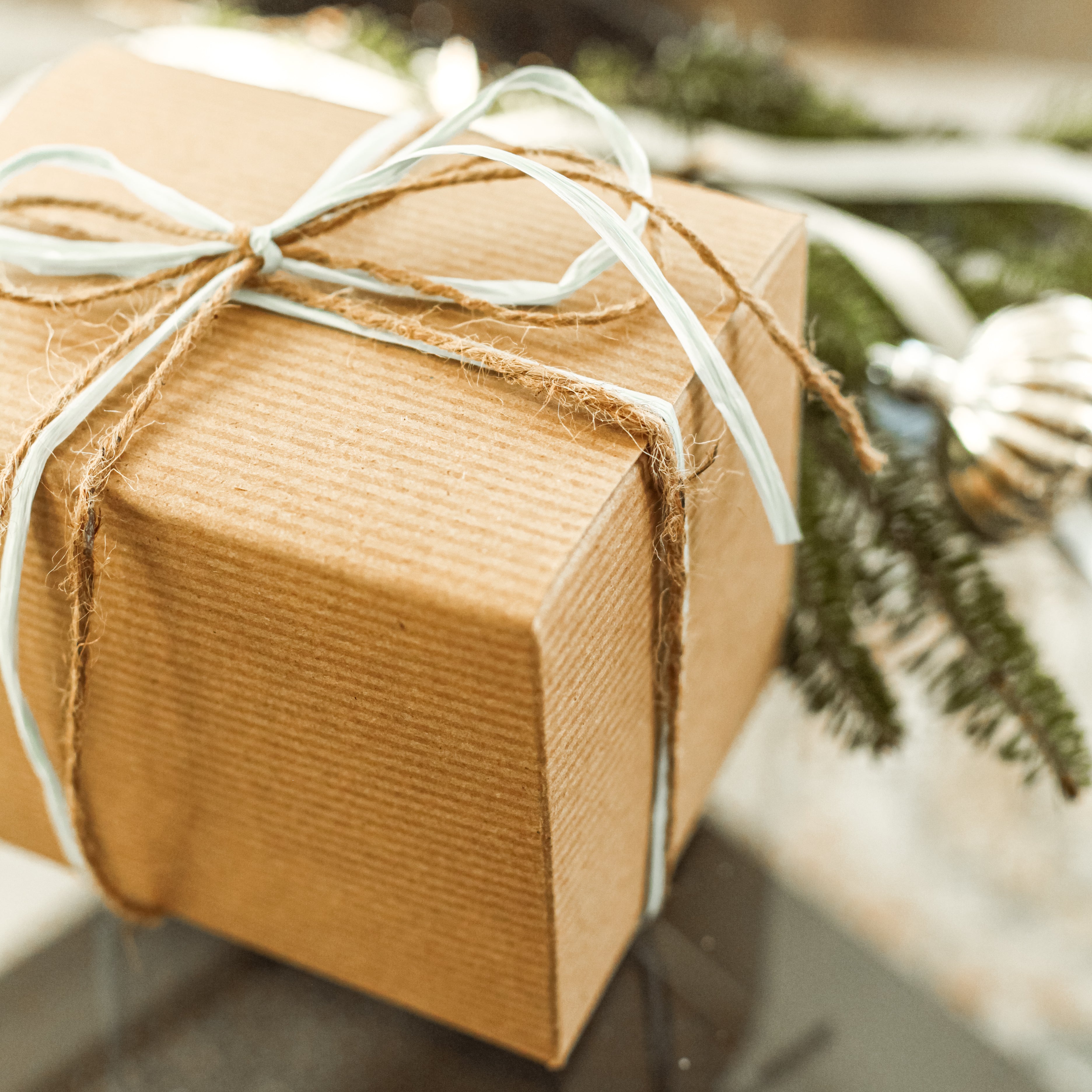 Brown paper-wrapped gift with string, blurred Christmas tree in the background