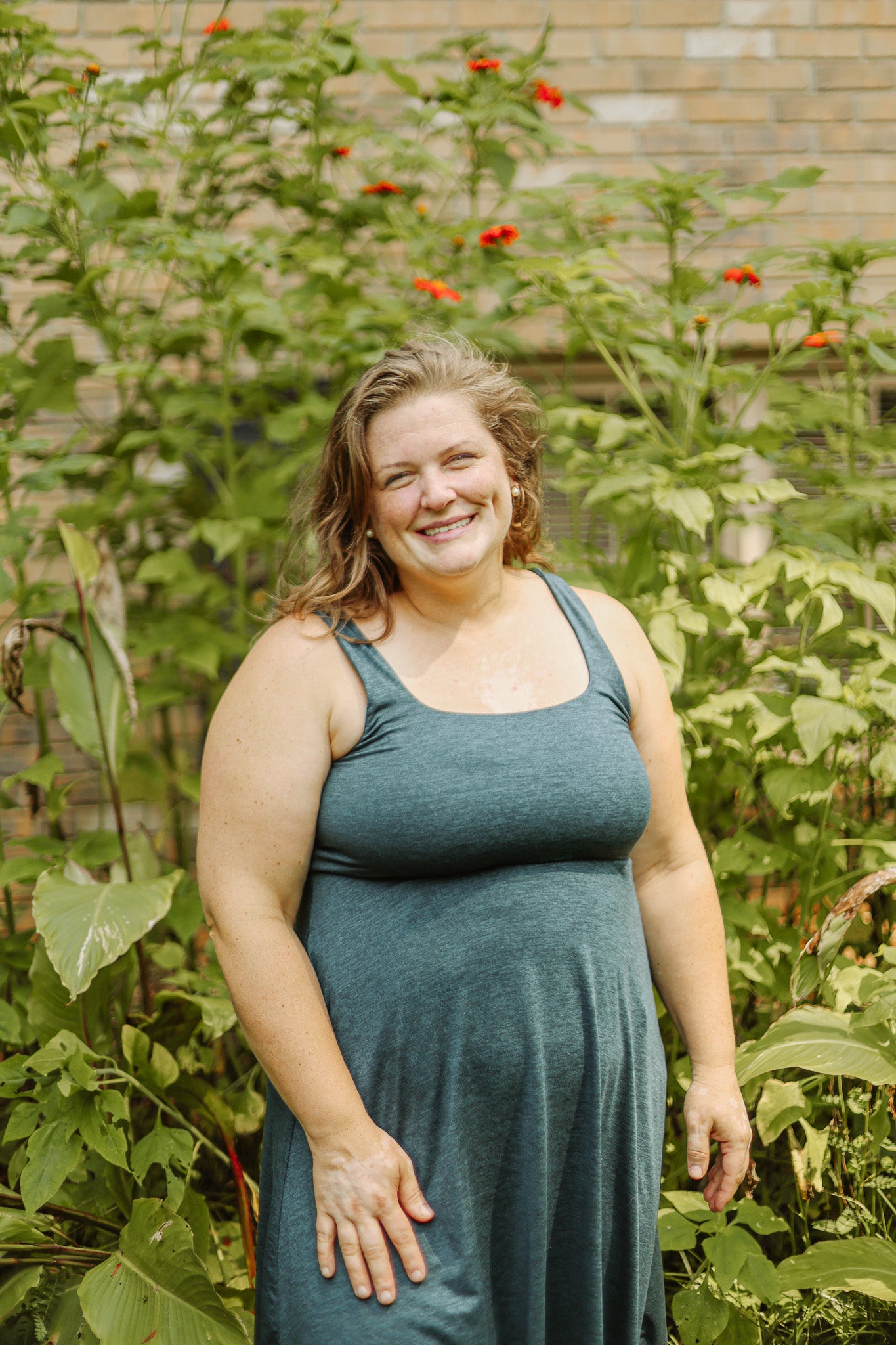 Cassie in a green dress standing in a garden with plants and flowers around her.