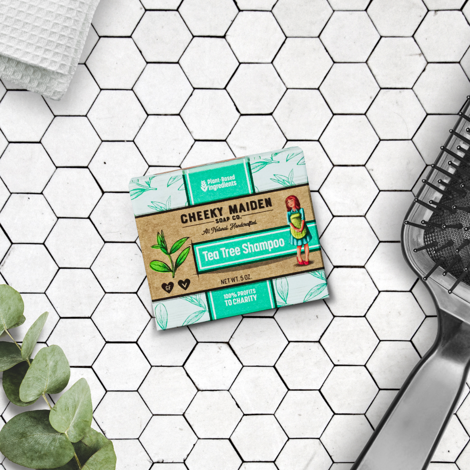 Cheeky Maiden Tea Tree Shampoo bar on a tiled bathroom floor with a plant and loofah.